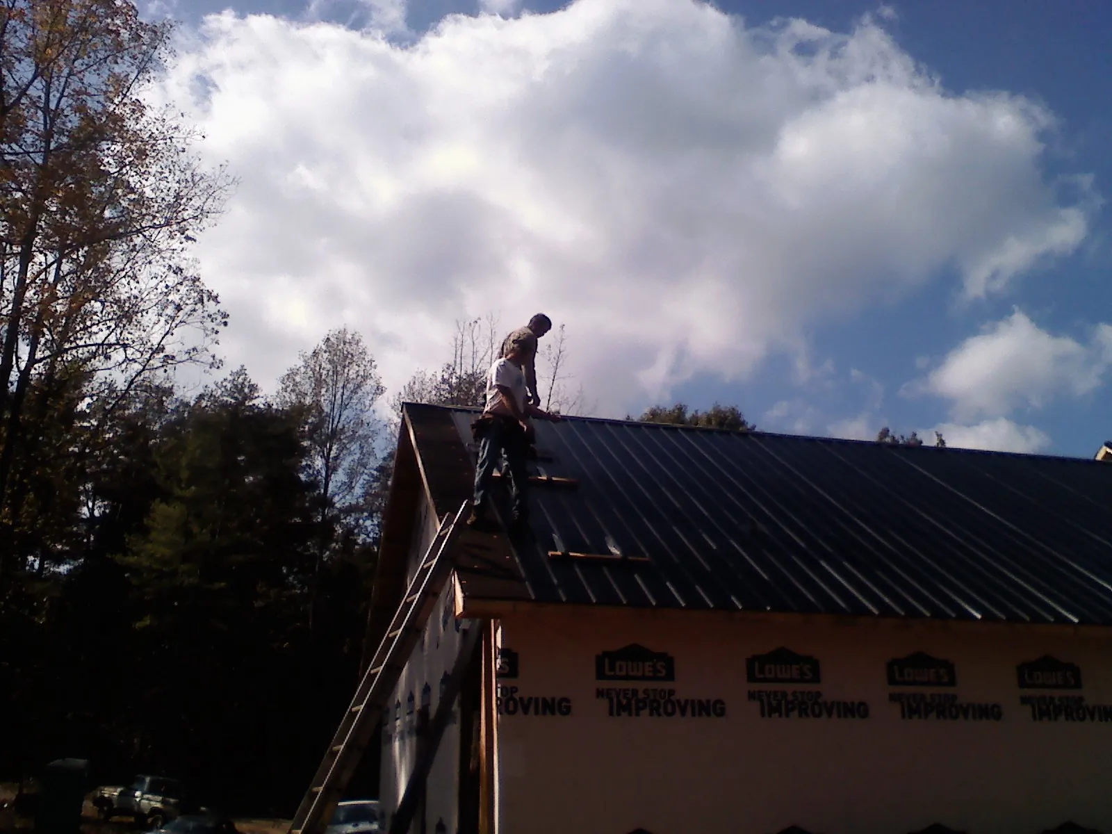 Roofer fastening dark metal panels high against a cloudy sky, from a Roof Inspection job in Tabernash